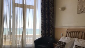 A hotel room with a large bed, a chair, and a view of the sea through sheer curtains. - The Lindum (Hastings)