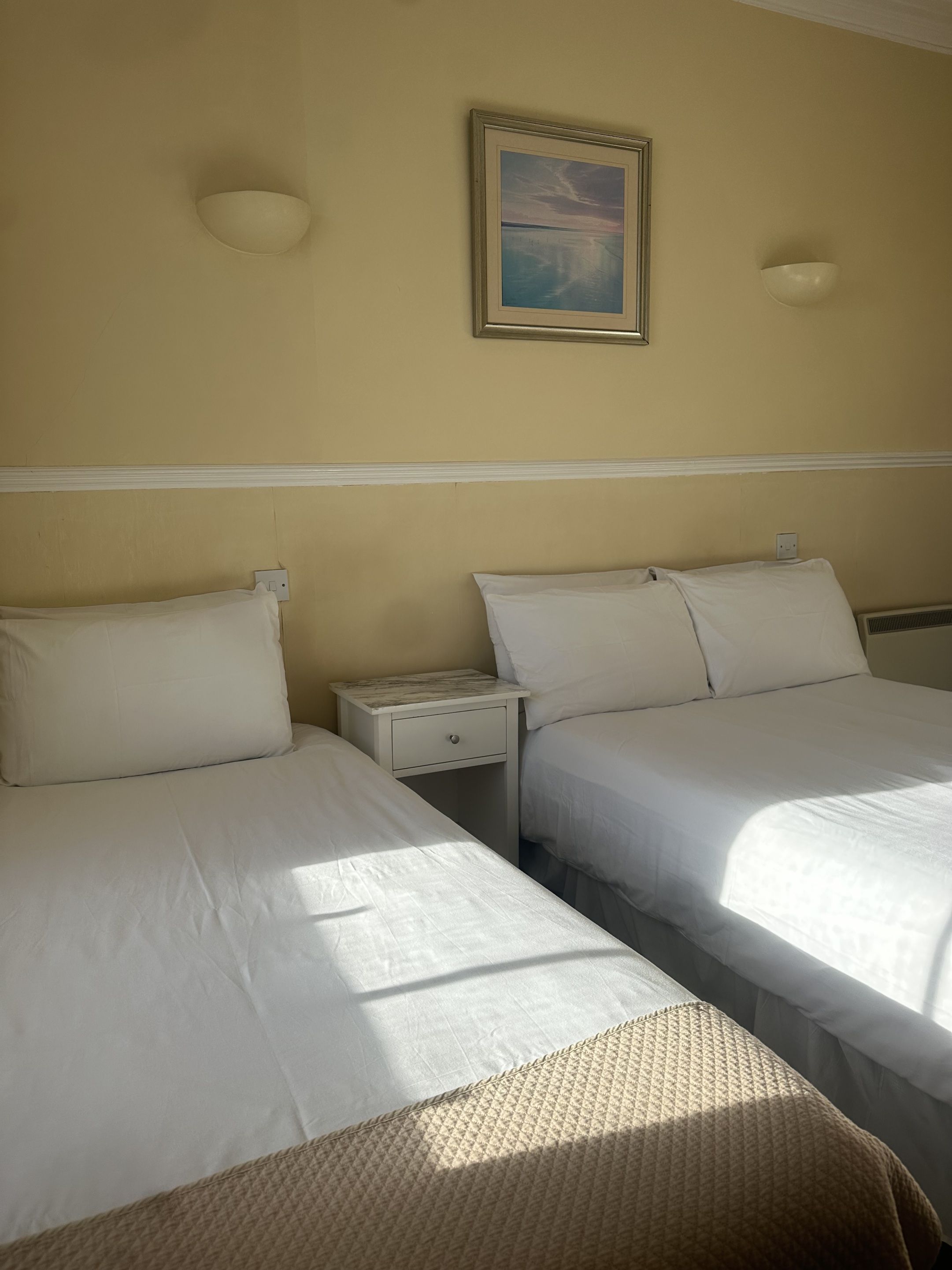 Una habitación de hotel con dos camas, una mesita de noche, una lámpara de pared y un cuadro enmarcado.