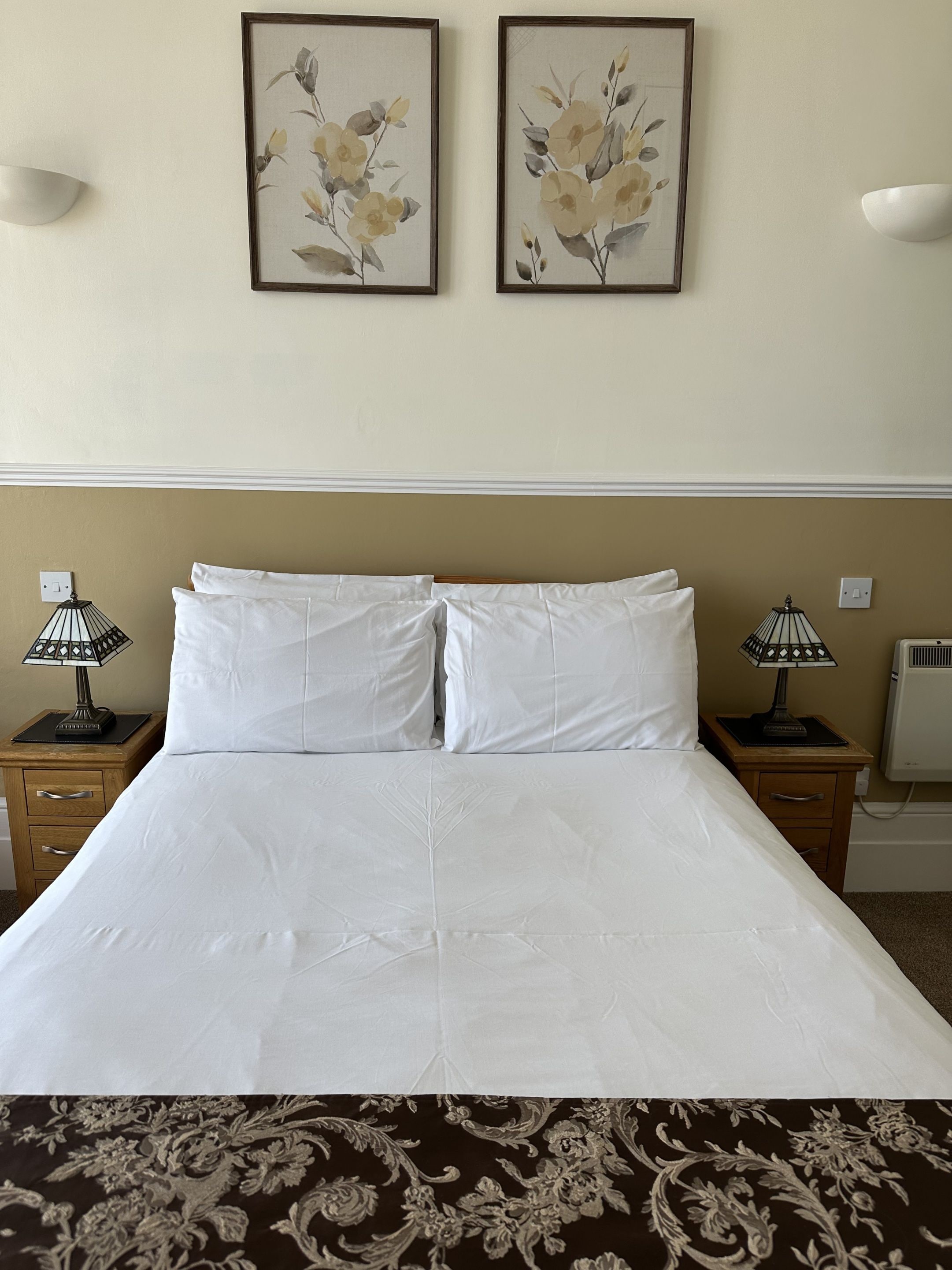 A hotel room with a bed, two nightstands, two wall-mounted lamps, and two framed floral paintings.