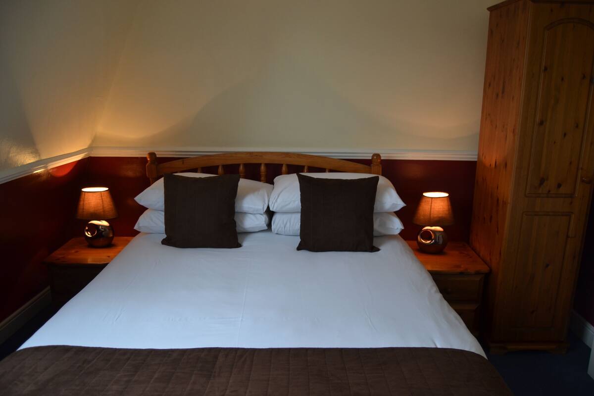 A neatly made bed with white and brown bedding, flanked by two bedside lamps on wooden nightstands.