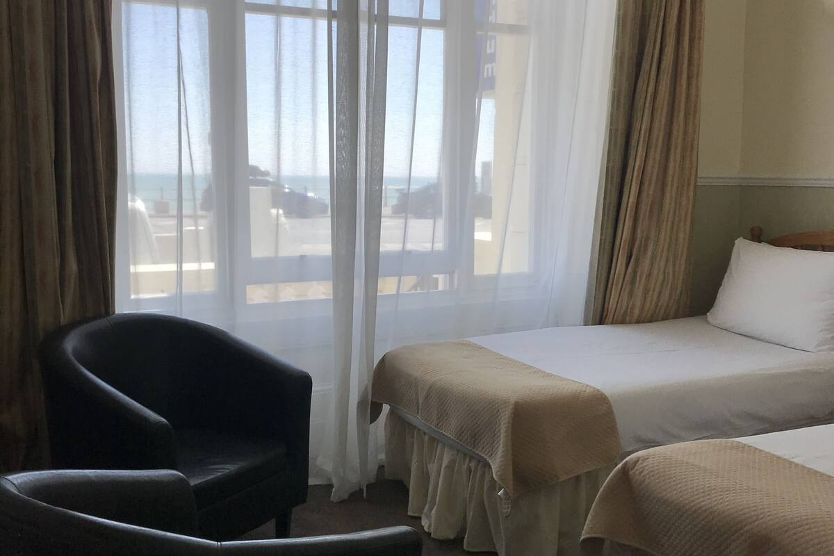 A hotel room with two beds, a chair, and a large window with curtains.