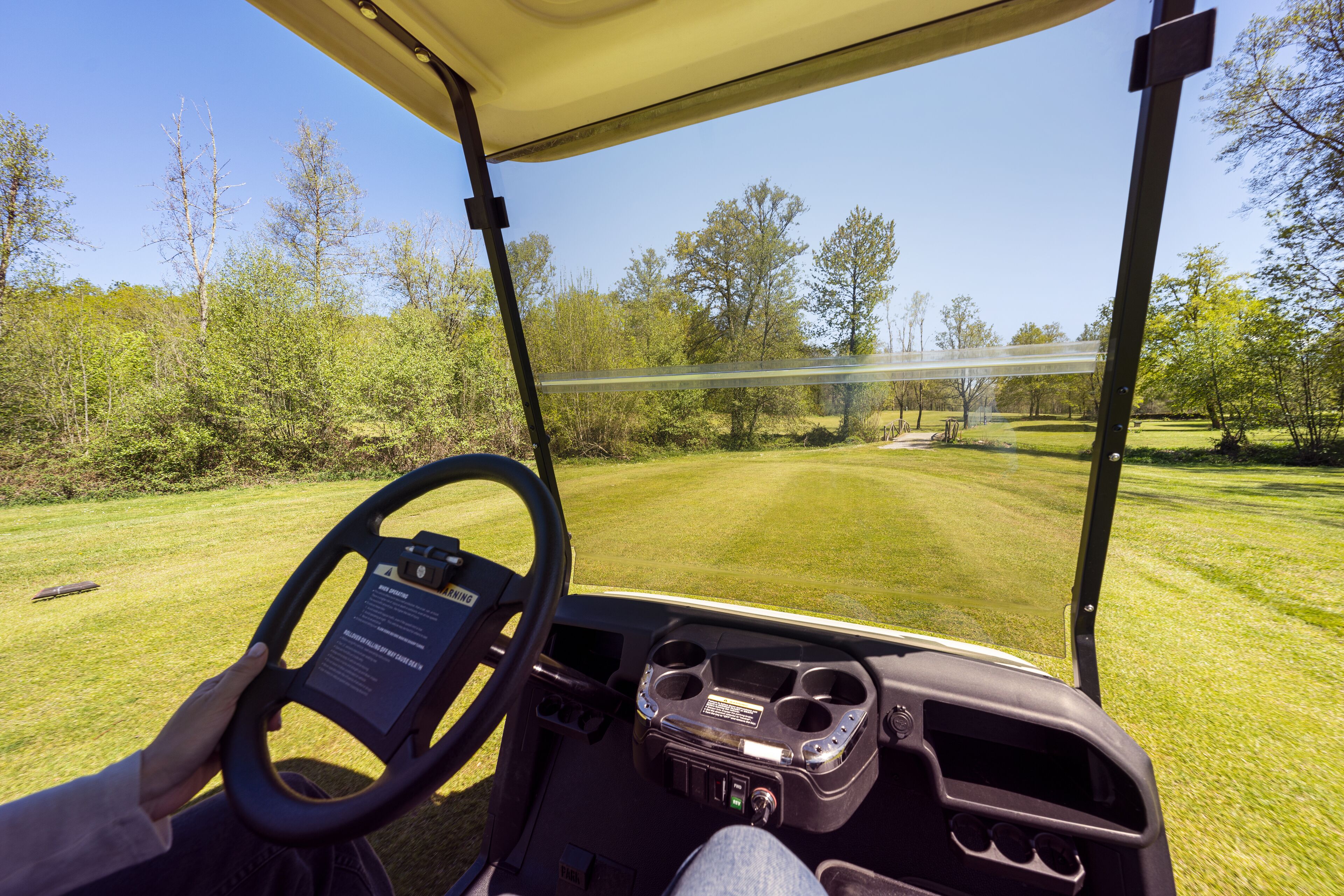 A golf cart interior with a steering wheel, dashboard, and cup holders.