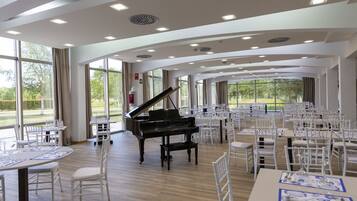Un salón amplio con un piano de cola, sillas blancas y mesas dispuestas para cenar.
