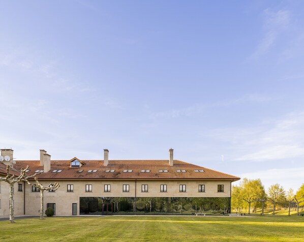 A large building with a tiled roof, multiple windows, and a grassy courtyard.