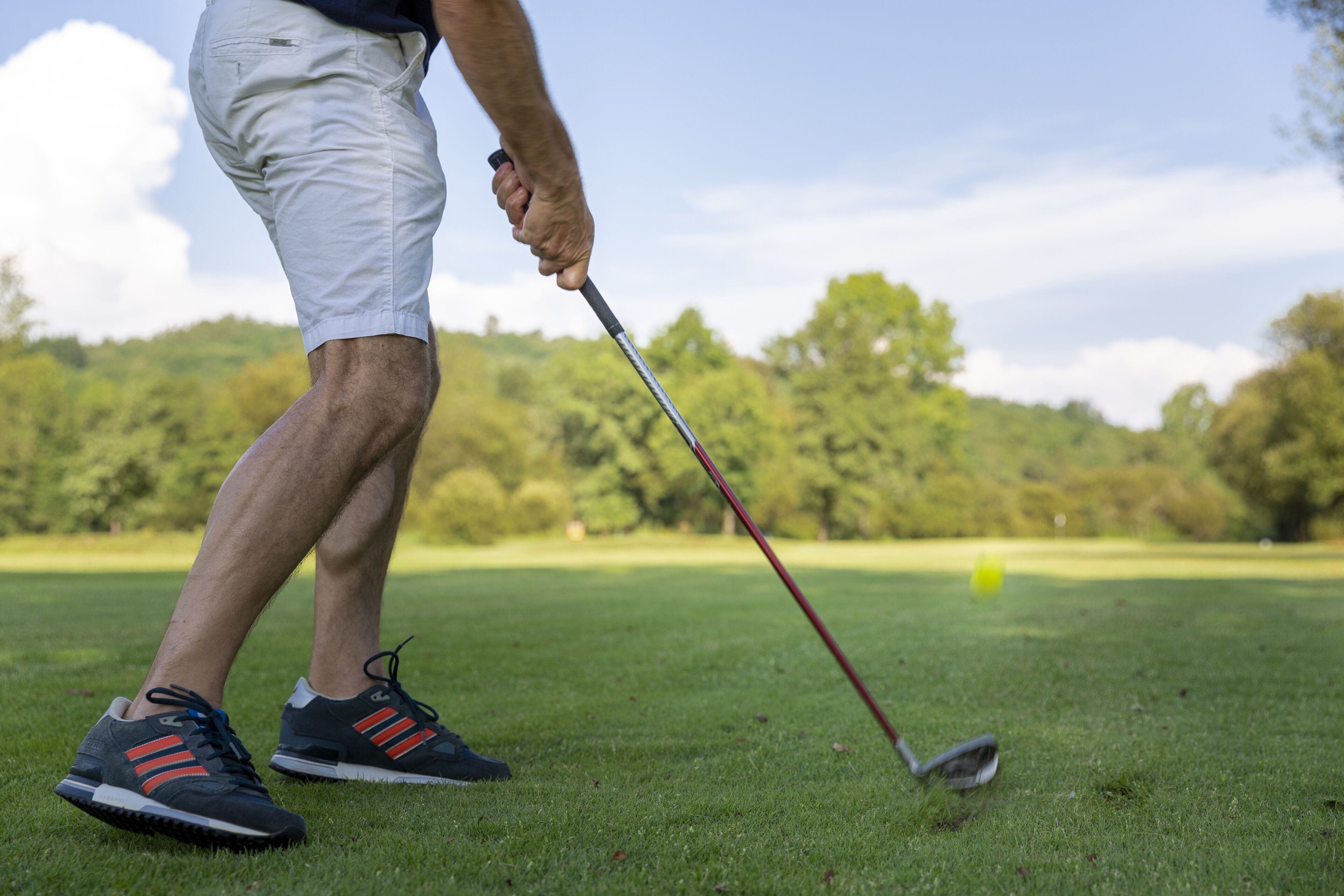 Una persona con pantalones cortos y zapatillas de deporte en un campo de golf, sosteniendo un palo de golf.