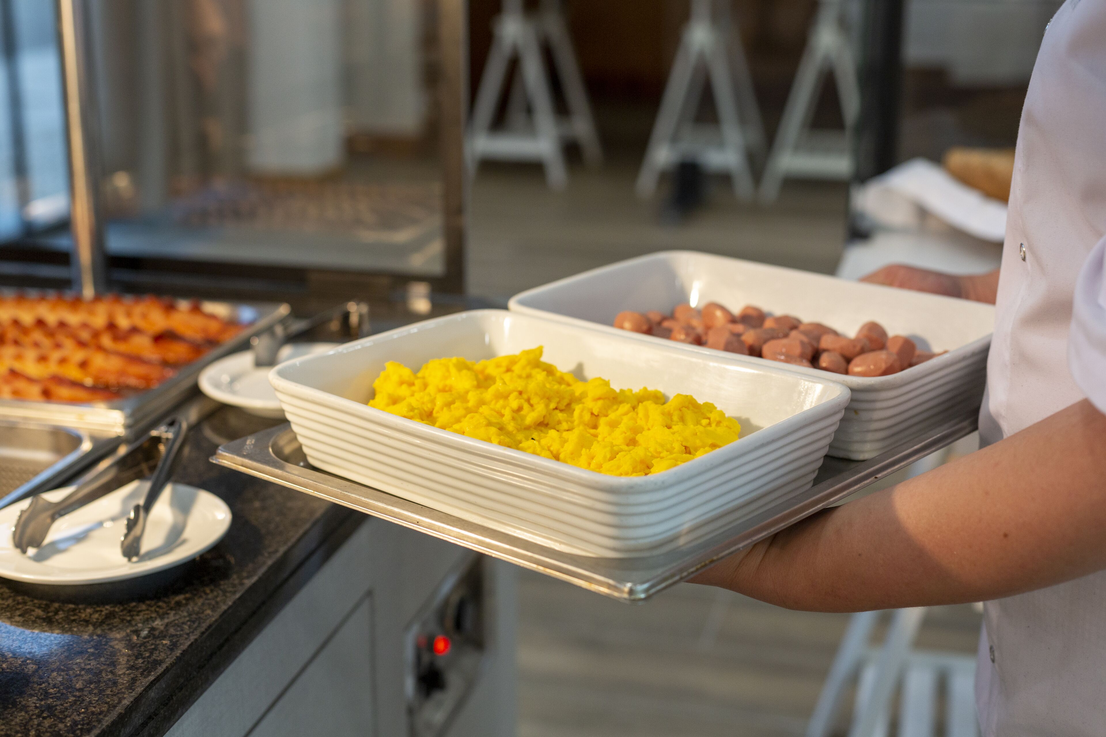 Een buffetopstelling met schalen vol eten, waaronder gele rijst en bruine worsten, in een keukenruimte.