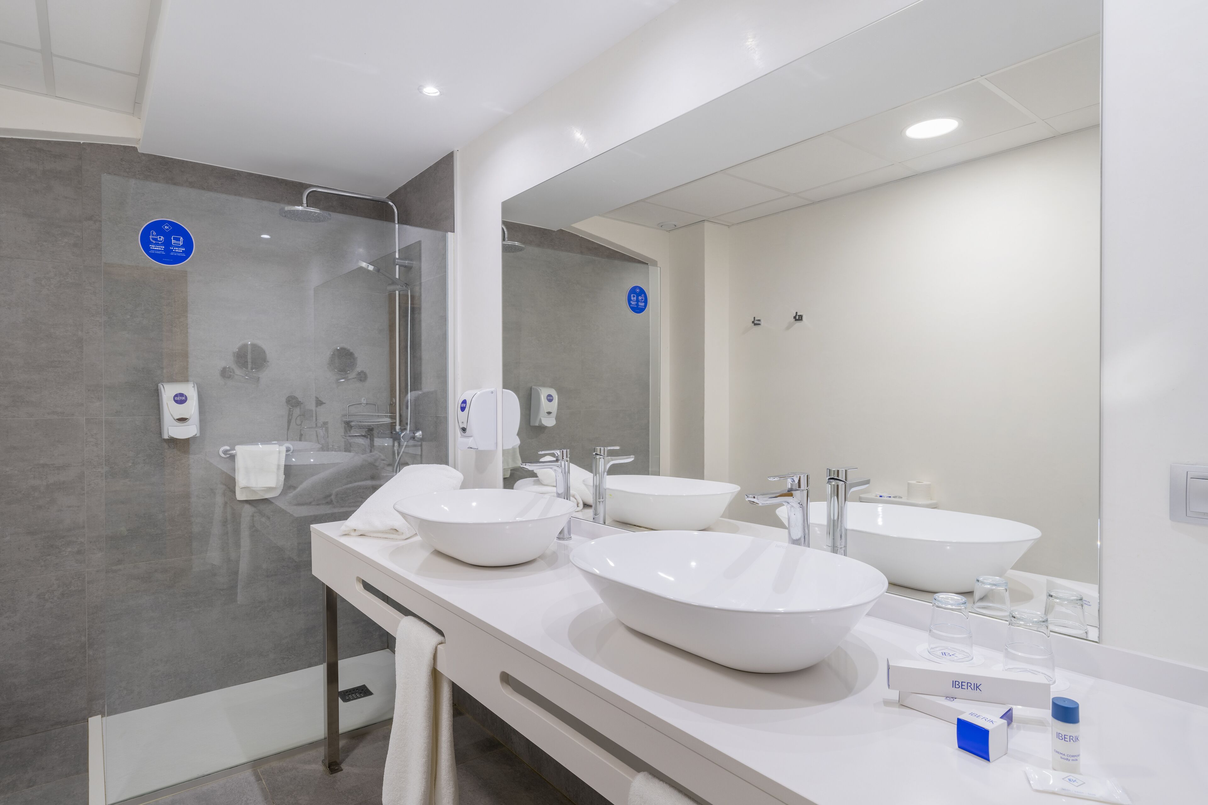 A modern bathroom with two large white sinks, a glass shower enclosure, and a large mirror.