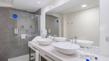 Un baño moderno con dos lavamanos grandes blancos, un box de ducha de cristal y un espejo amplio.