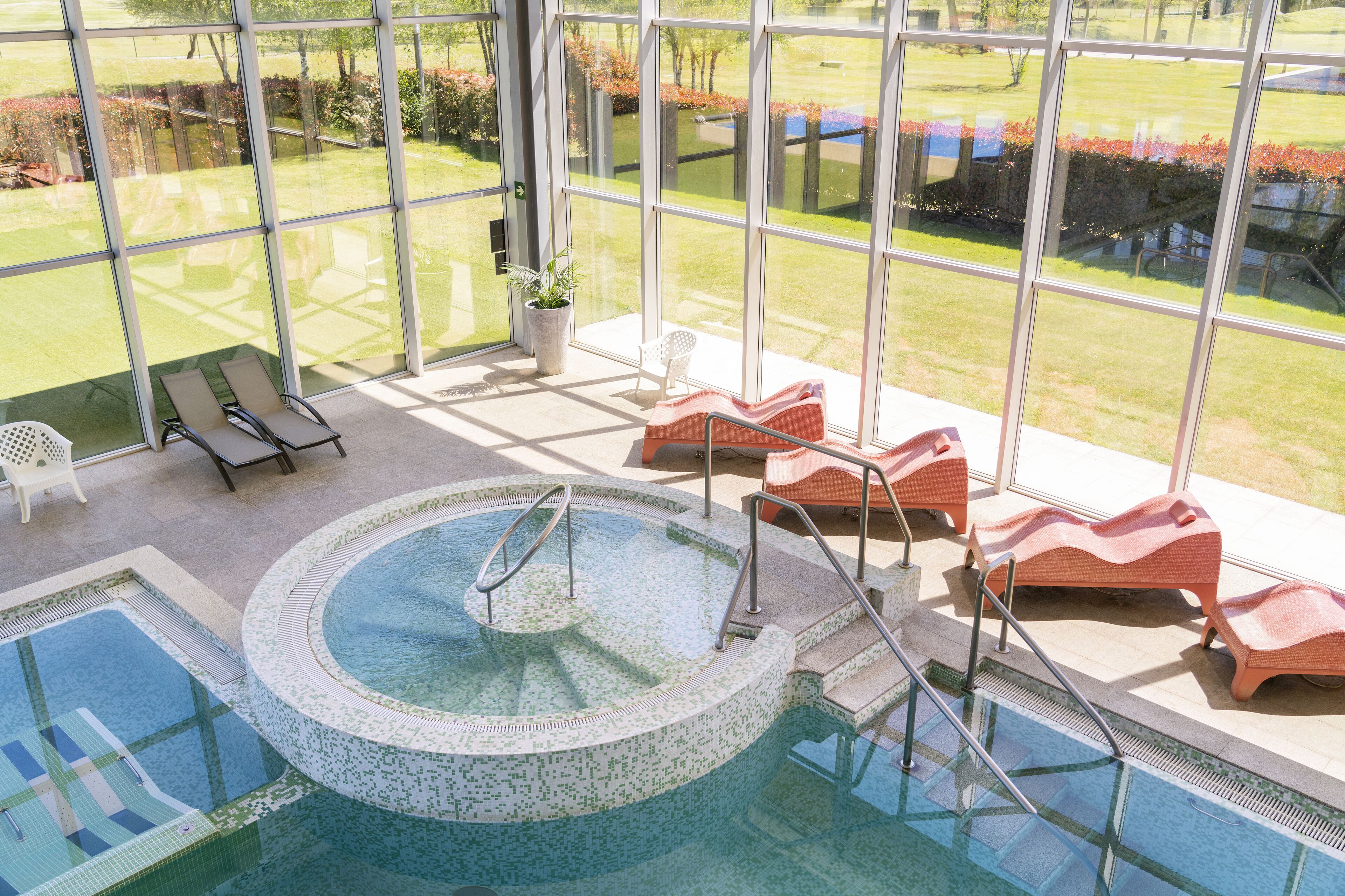 Un espace piscine doté d’un jacuzzi, de chaises longues et offrant une vue sur un jardin grâce à de grandes fenêtres.