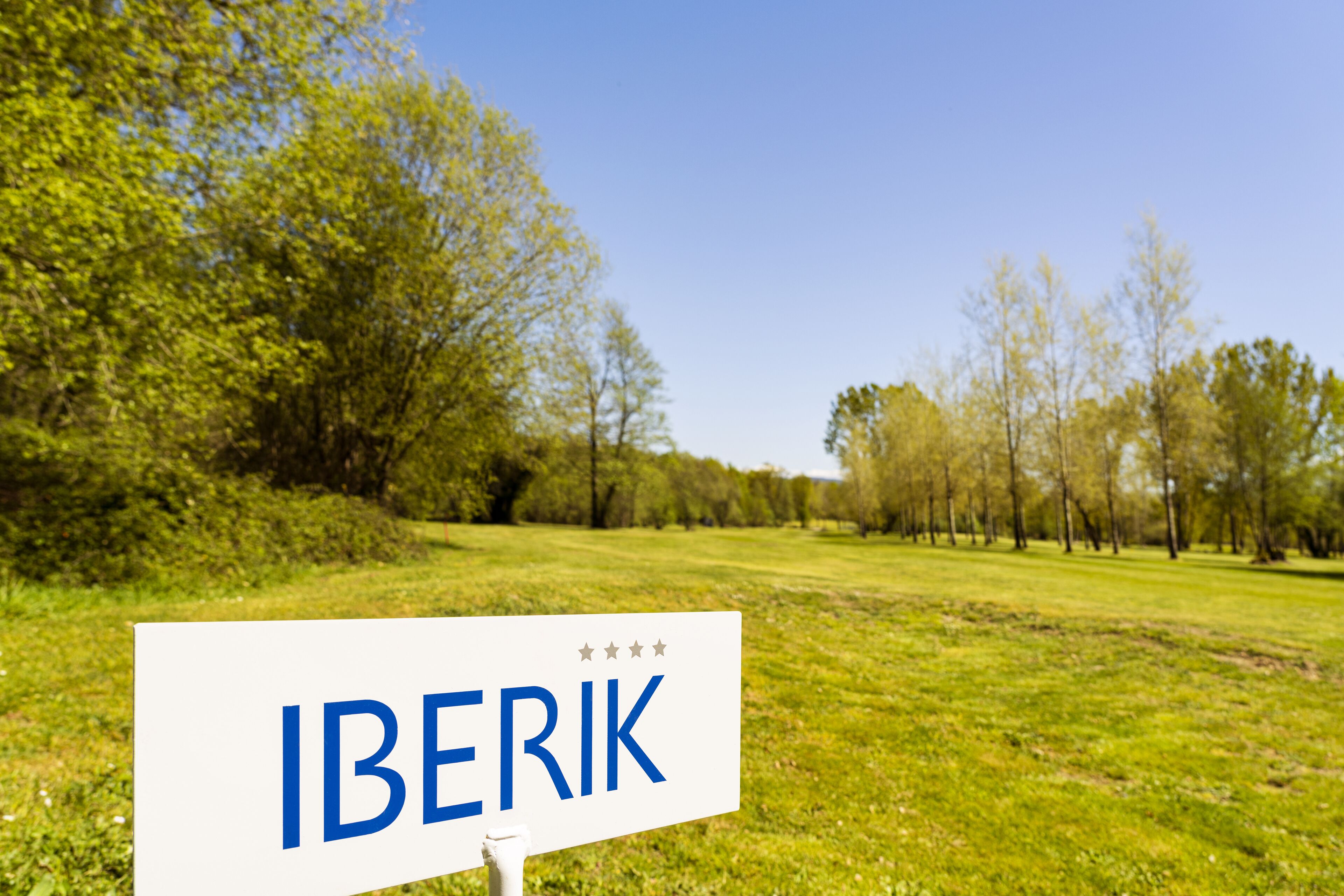 Un panneau sur lequel est écrit le mot « IBERIK », placé dans un champ avec des arbres et de l’herbe.