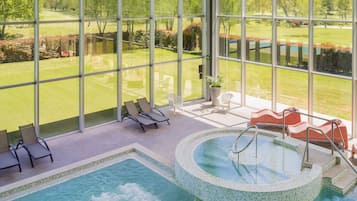 Zona de piscina con sillones de descanso, un jacuzzi y vistas a un campo de golf a través de amplias ventanas.