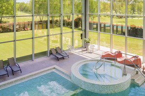 Een zwembadgedeelte met ligbedden, een jacuzzi en uitzicht op een golfbaan door grote ramen.
