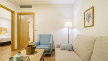 A room with a bed, a blue armchair, a beige sofa, a wooden table with vases, and a floor lamp.
