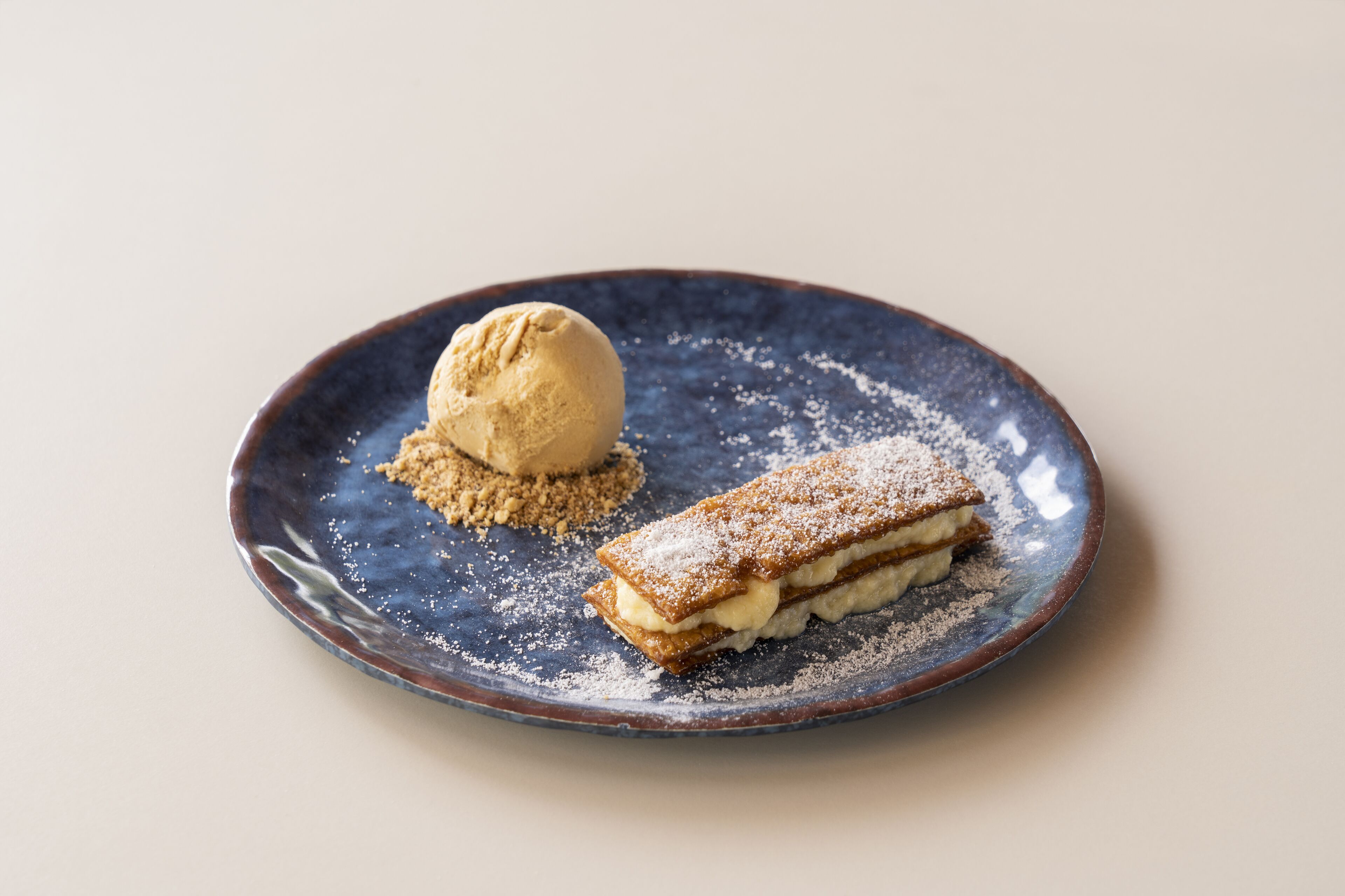 Dessert auf einem Keramikteller mit einer Kugel Eis und Blätterteig.
