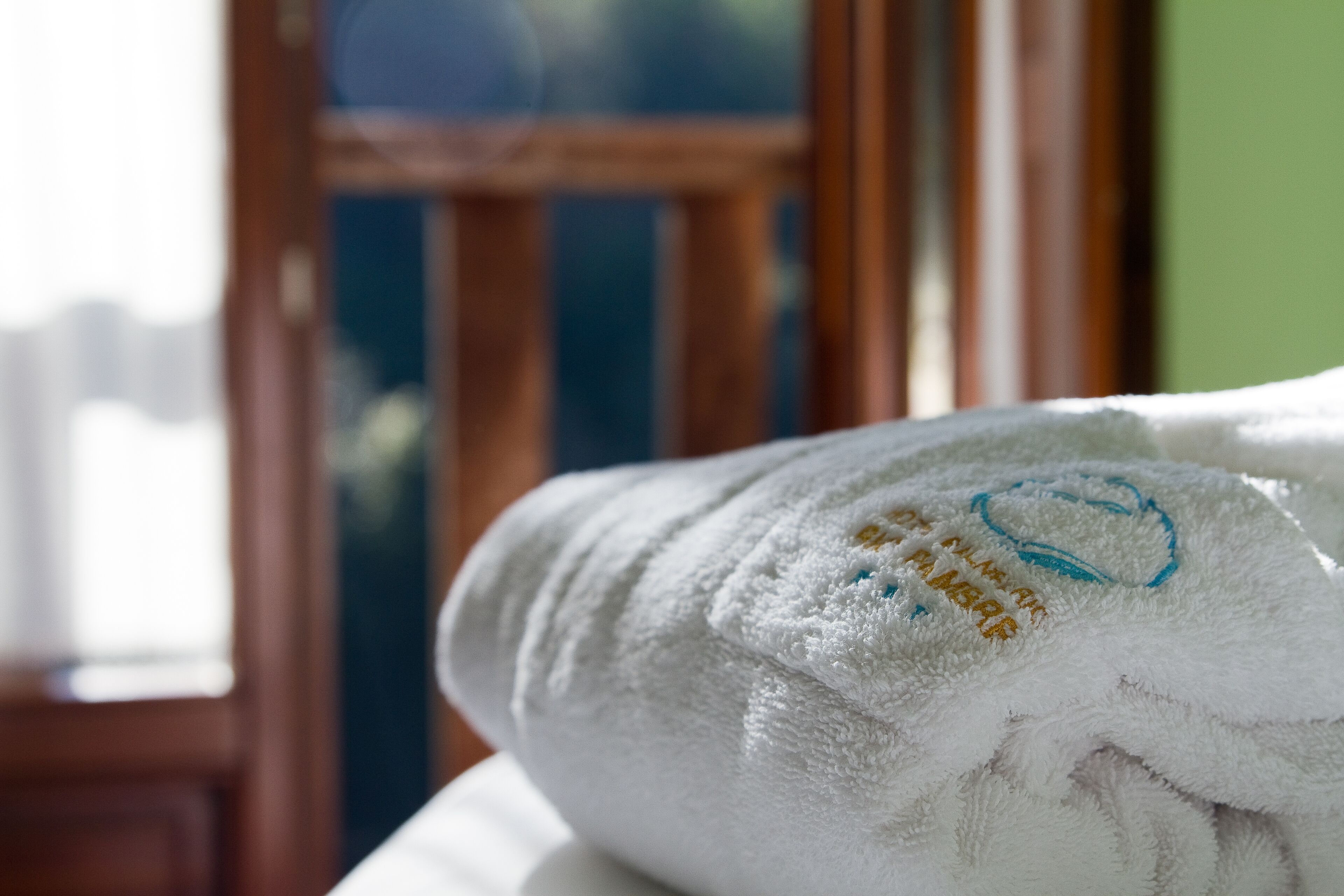 A white towel with embroidered text and a blue logo, placed on a surface with a window in the background.