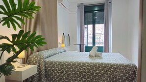 A neatly arranged hotel room with a bed, a bedside lamp, a potted plant, and a window with curtains. - CH Rayuela (Madrid)