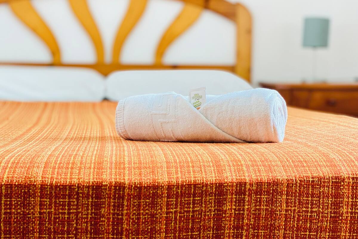 A neatly made bed with a rolled towel on the bed.
