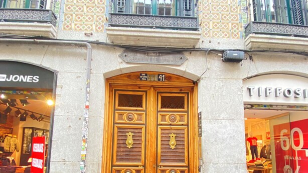 A building with a large wooden double door, a sign reading "Asegurada de Incendios", and storefronts for "Jones" and "Tiffosi". - CH Rayuela (Madrid)