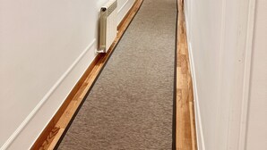 A long, narrow hotel corridor with white walls, wooden flooring, and a central carpeted path. - CH Rayuela (Madrid)