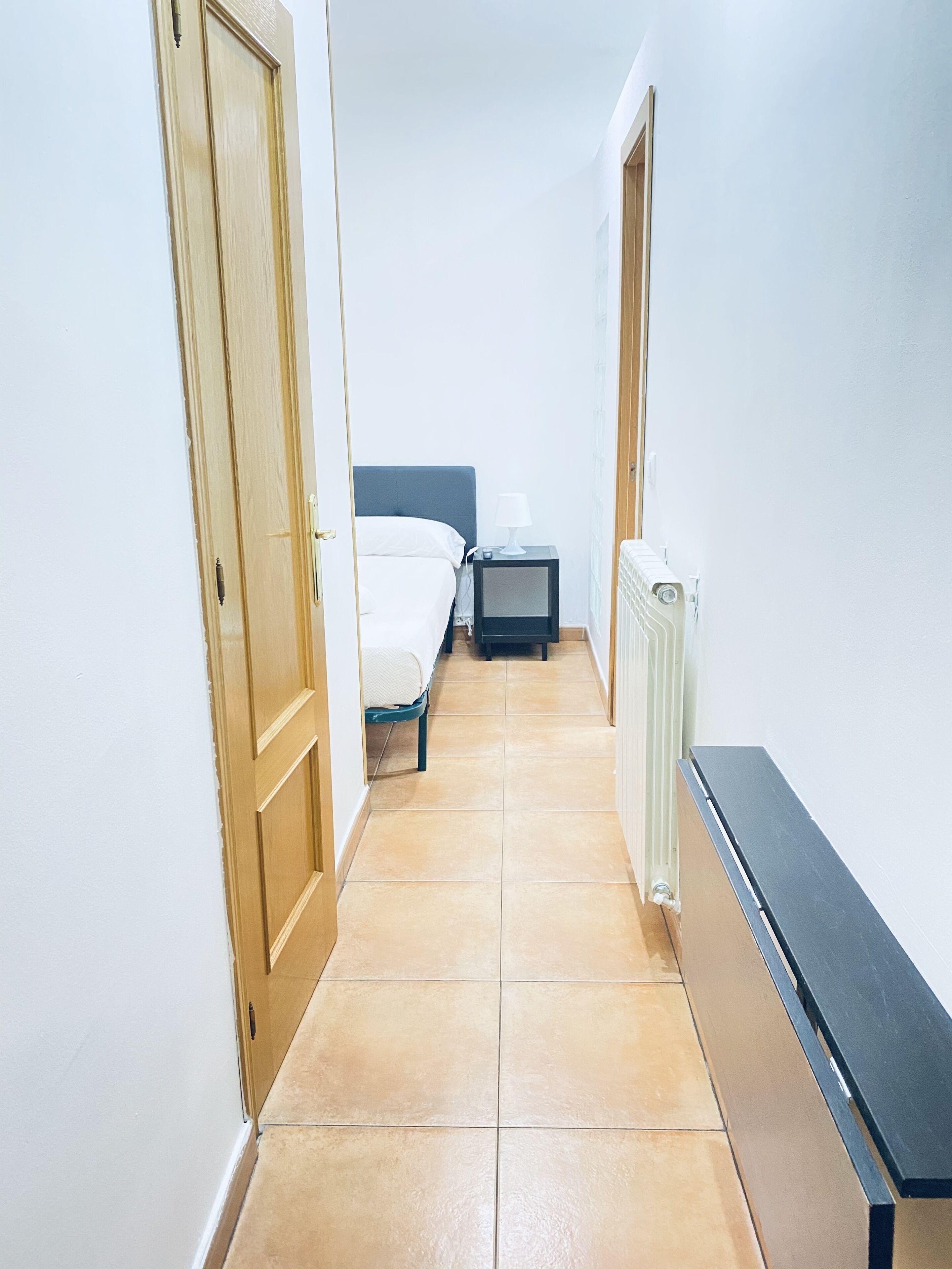 A narrow hallway with a bed, a nightstand, and a radiator.