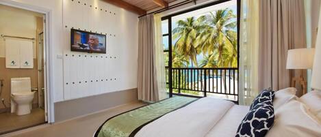 A hotel room with a bed, a TV mounted on the wall, a balcony with a view of palm trees, and a ceiling fan.