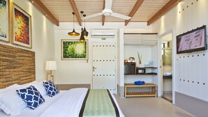 A hotel room with a bed, a ceiling fan, a TV, a door, and a small table with a lamp. - Crystal Sands (Maafushi)