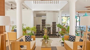 A spacious lobby with wicker furniture, a central water feature, and a view of the outdoor seating area. - Crystal Sands (Maafushi)