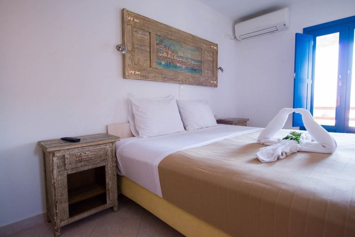 A bedroom with a bed, a nightstand, a wall-mounted painting, and a window with blue shutters.