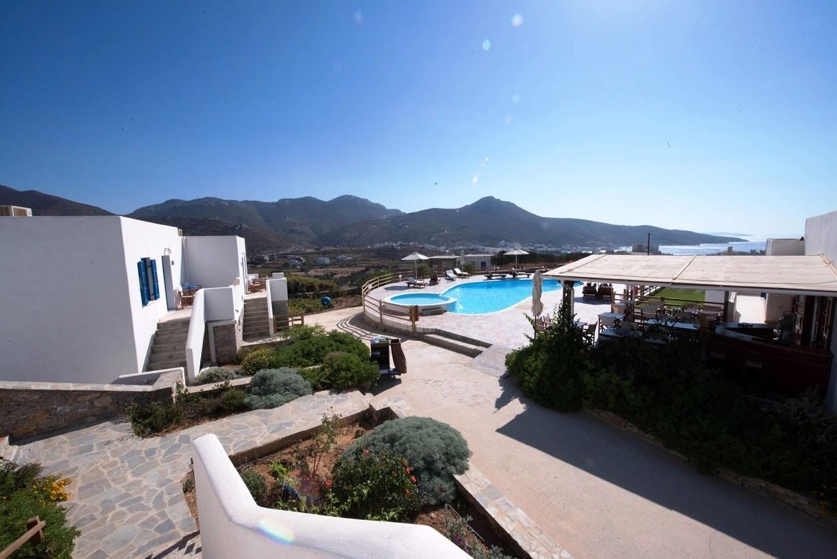 A pool area with a view of mountains, a covered seating area, and a white building with steps leading to the pool.