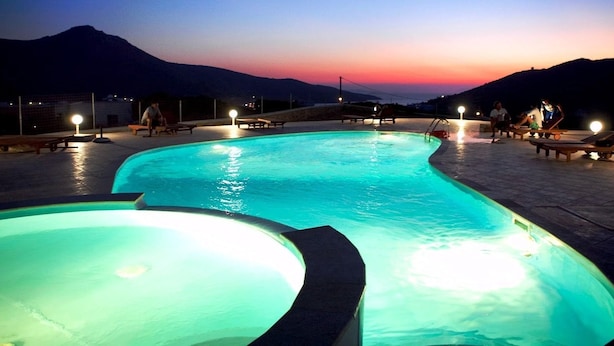 Une piscine à bordures courbes, entourée de chaises longues et de tables, avec en toile de fond un paysage montagneux baigné par la lumière du crépuscule.
