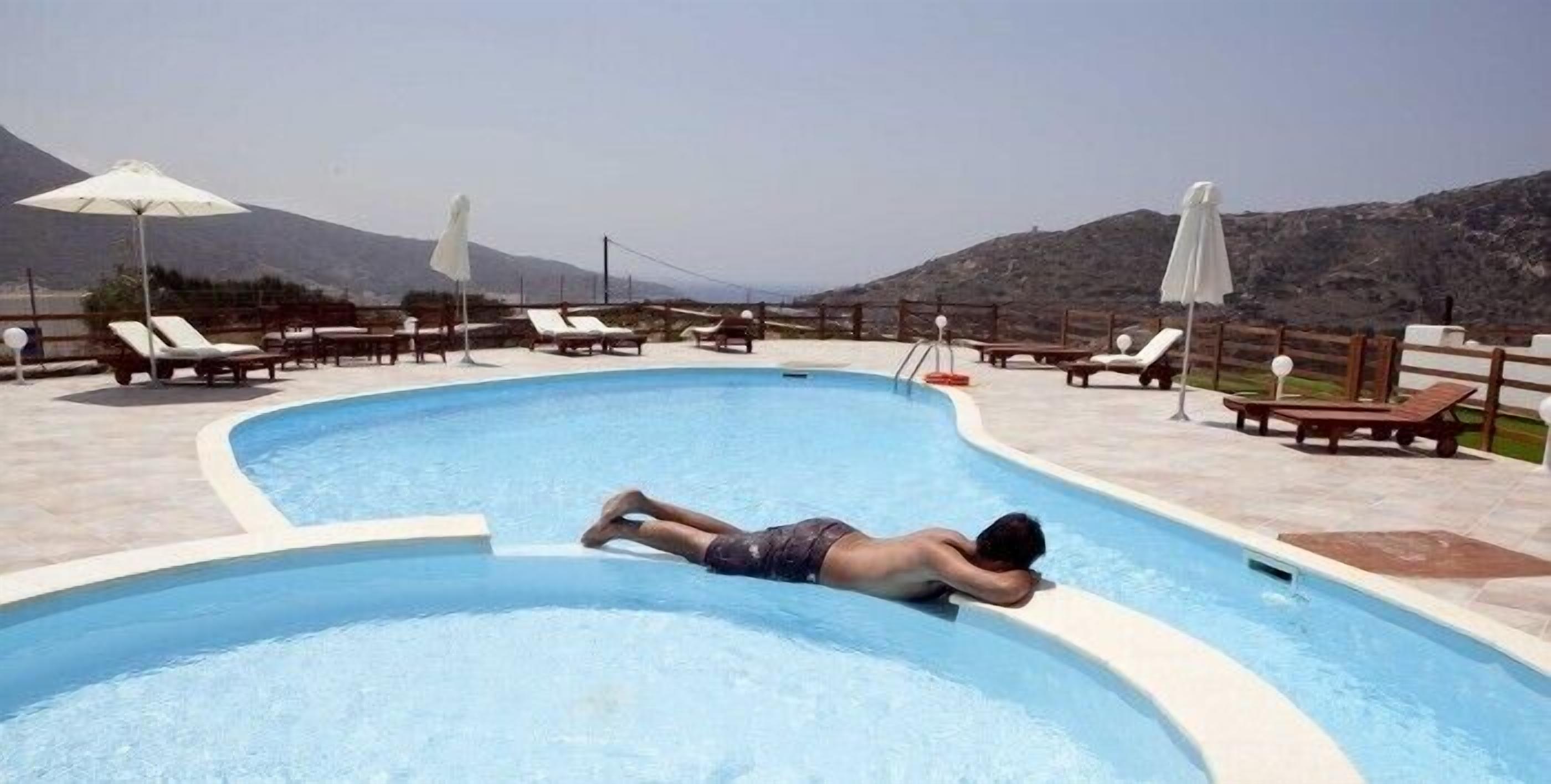 A pool area with lounge chairs and umbrellas, surrounded by a mountainous landscape.