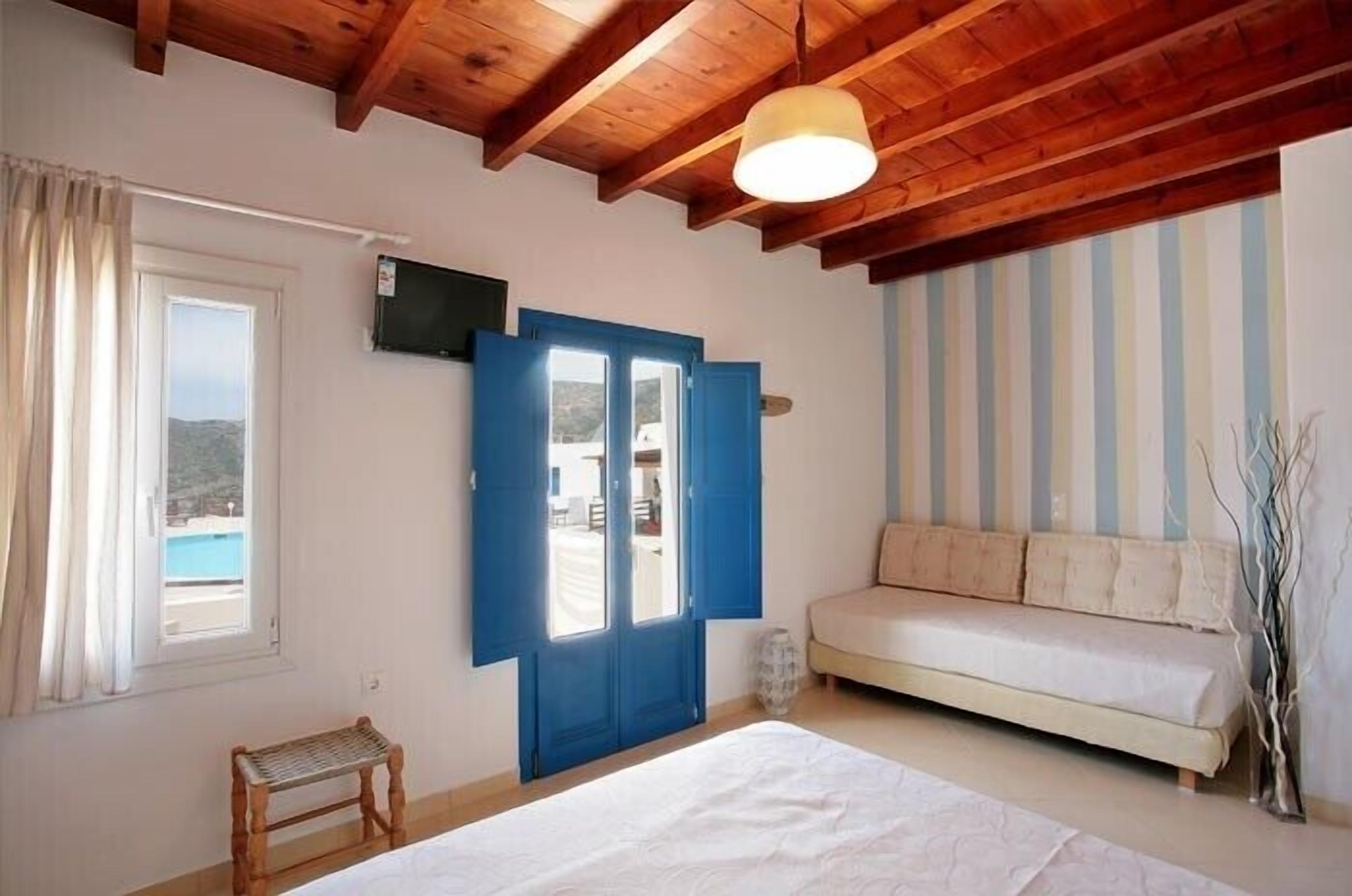 Una habitación con techo de madera, una cama, un sofá, un televisor y una ventana con cortinas.