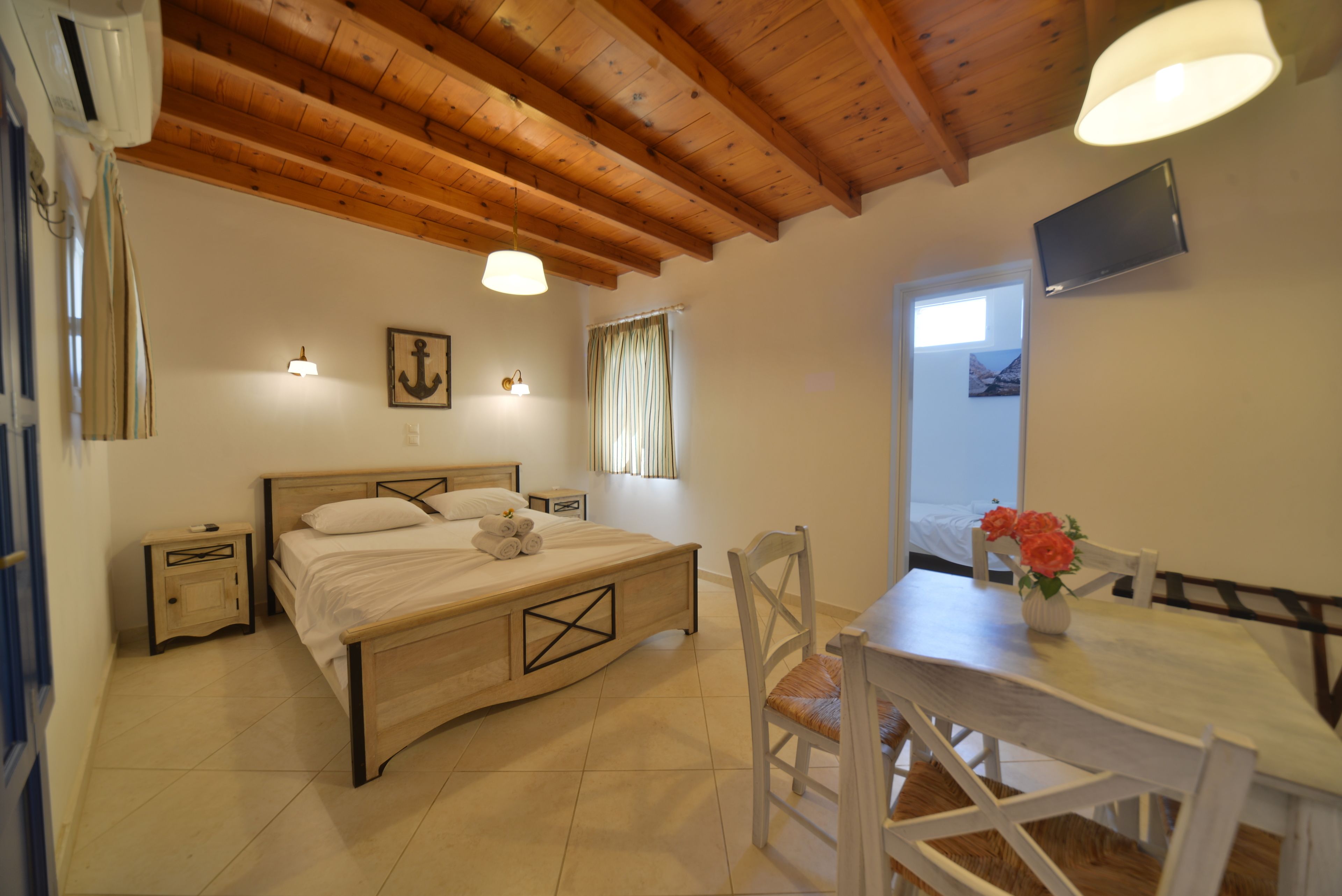 A bedroom with a wooden bed, bedside tables, a desk with a chair, a TV mounted on the wall, and a window with curtains.