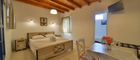 A bedroom with a wooden bed, bedside tables, a desk with a chair, a TV mounted on the wall, and a window with curtains.