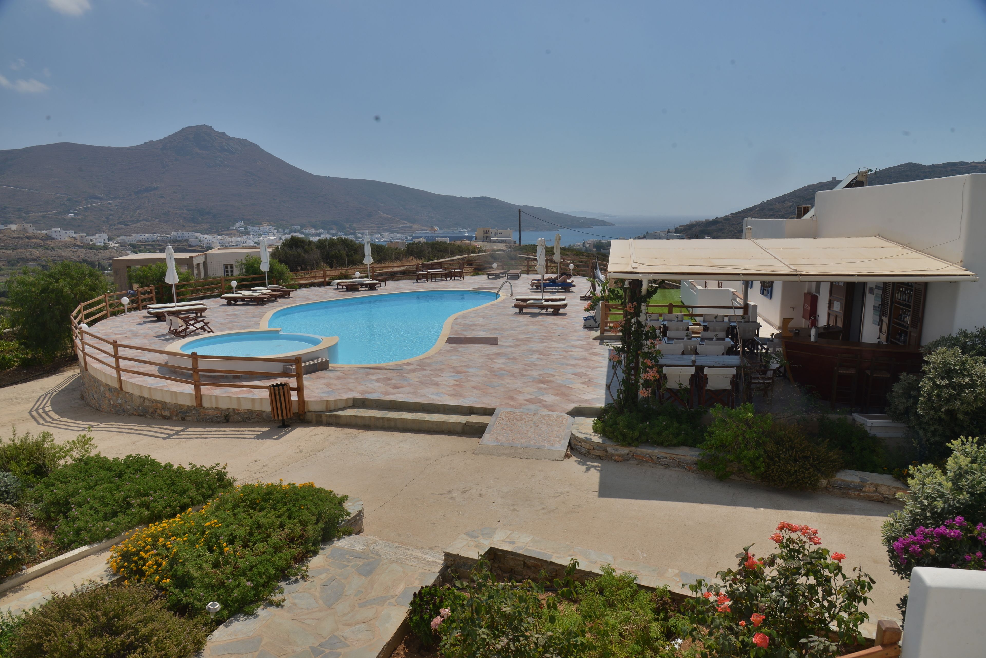 A pool area with a view of the sea and mountains, surrounded by outdoor seating and a garden.
