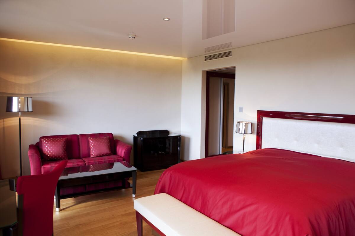 Une chambre d’hôtel moderne avec un grand lit, un canapé rouge, une petite table et un bureau.