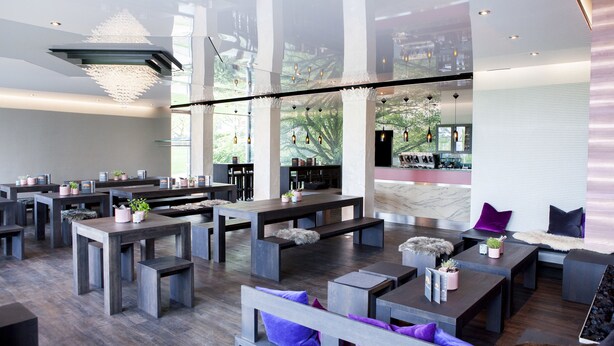 Un vaste espace intérieur aménagé avec différents types de sièges, notamment des tables et des bancs, et une grande fenêtre offrant une vue sur la verdure environnante.