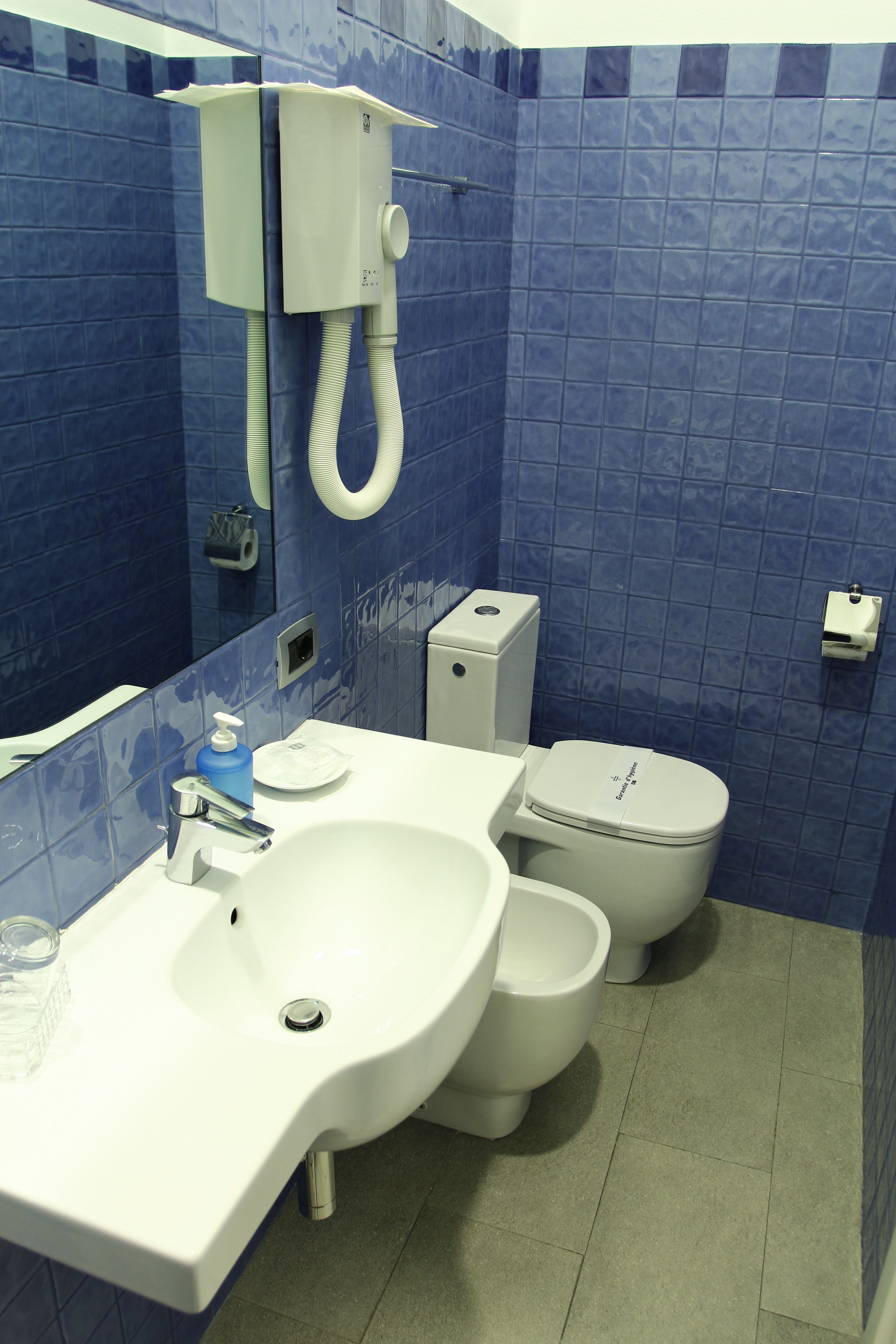 Un baño con un lavamanos blanco, dos inodoros y un espejo.
