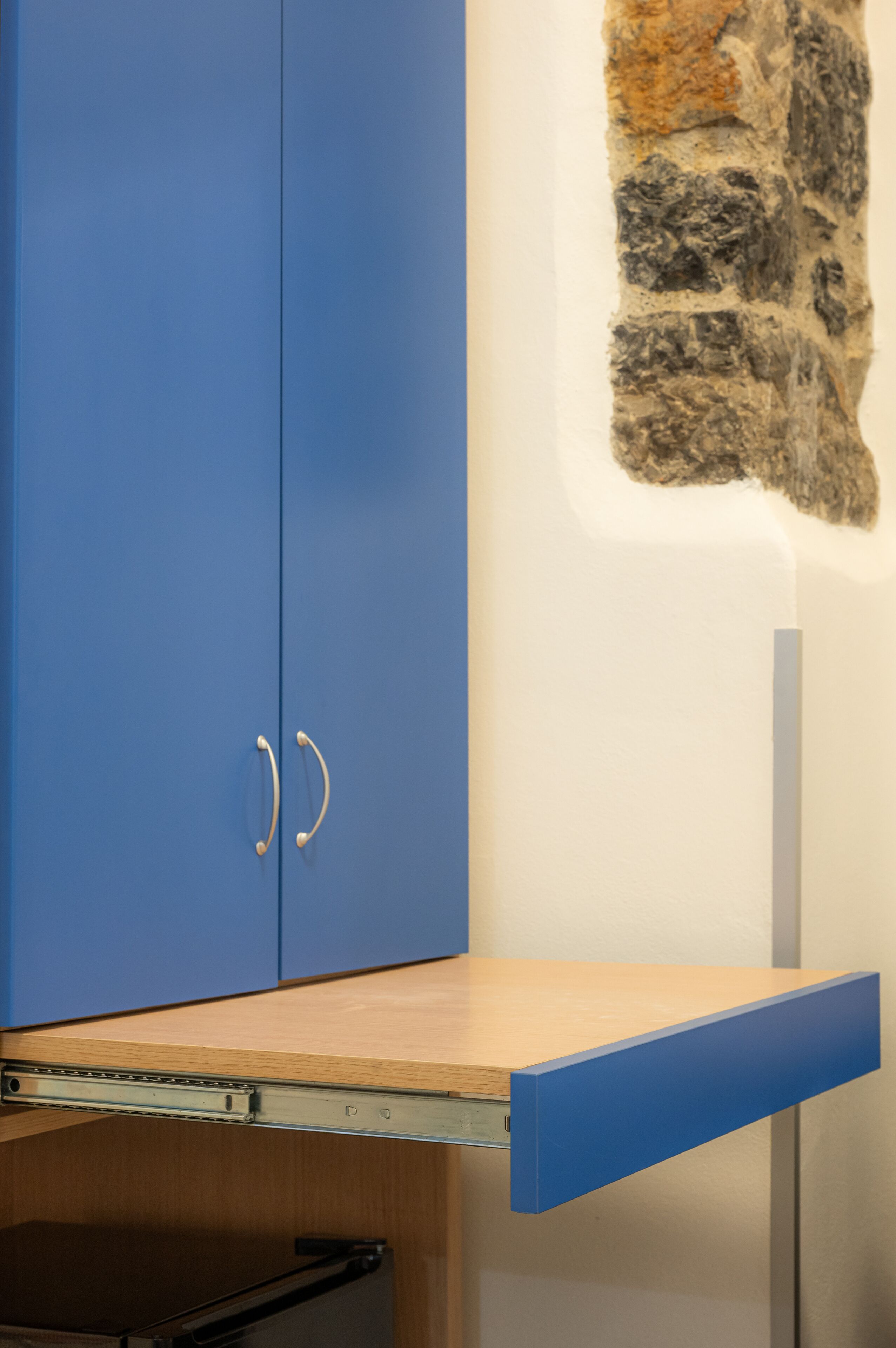 Un meuble bleu avec une étagère en bois, un mur en pierre et un support métallique.