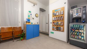 A reception area with a blue counter, a clock, a vending machine, and a bulletin board with various notices. - Affittacamere del Golfo e delle Cinque Terre (La Spezia)