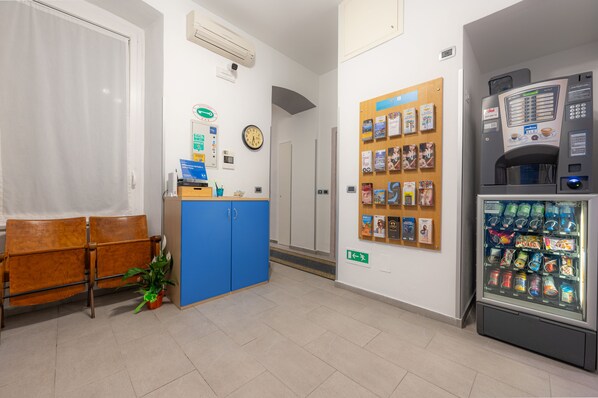 A reception area with a blue counter, a clock, a vending machine, and a bulletin board with various notices. - Affittacamere del Golfo e delle Cinque Terre (La Spezia)