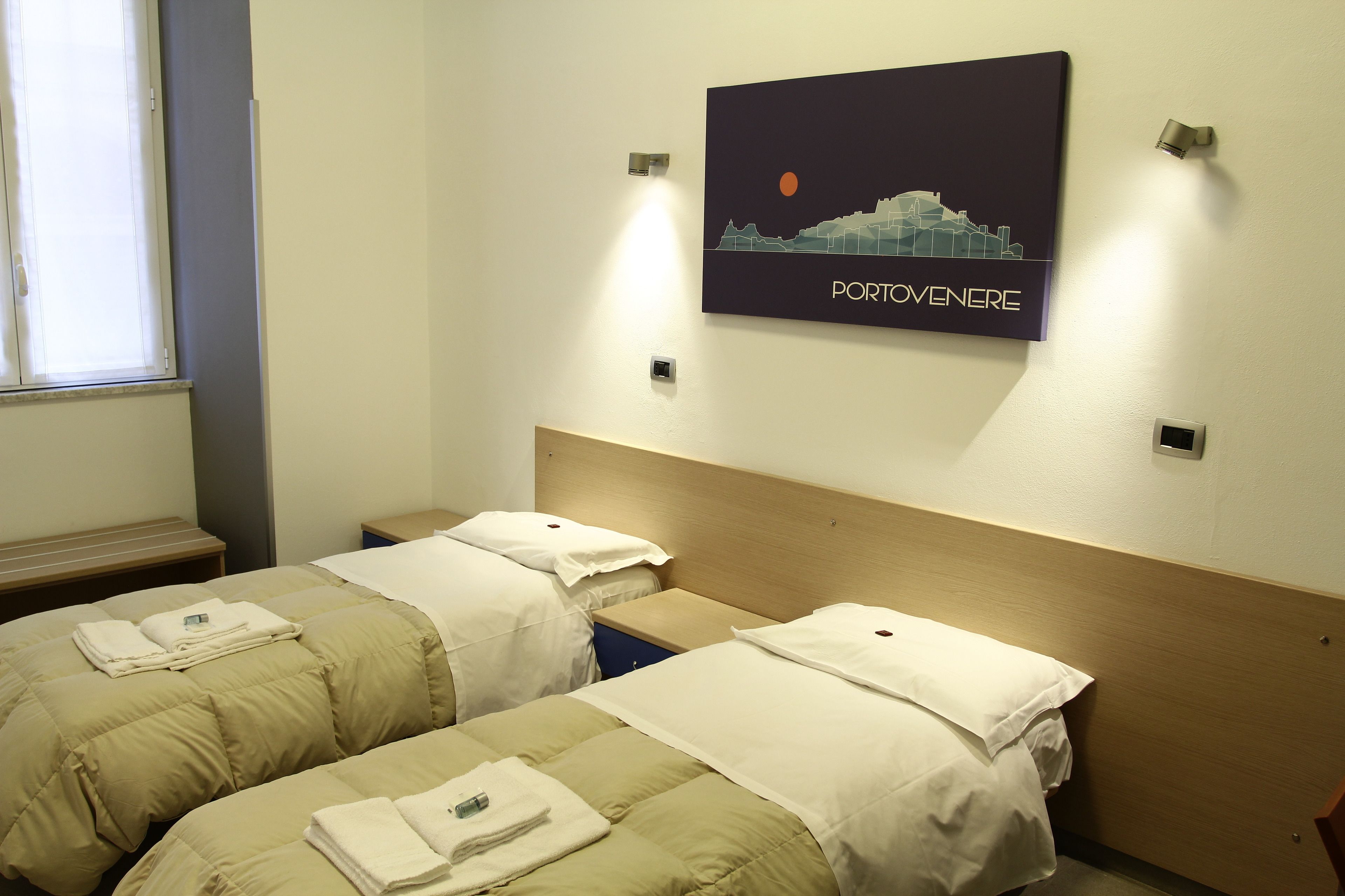 Ein Hotelzimmer mit zwei Betten, einem Nachttisch, einem Wandbild und einem Fenster.