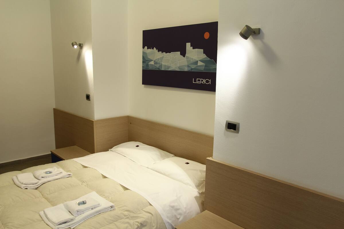 A hotel room with a bed, a wall-mounted artwork depicting a cityscape, and a night light.