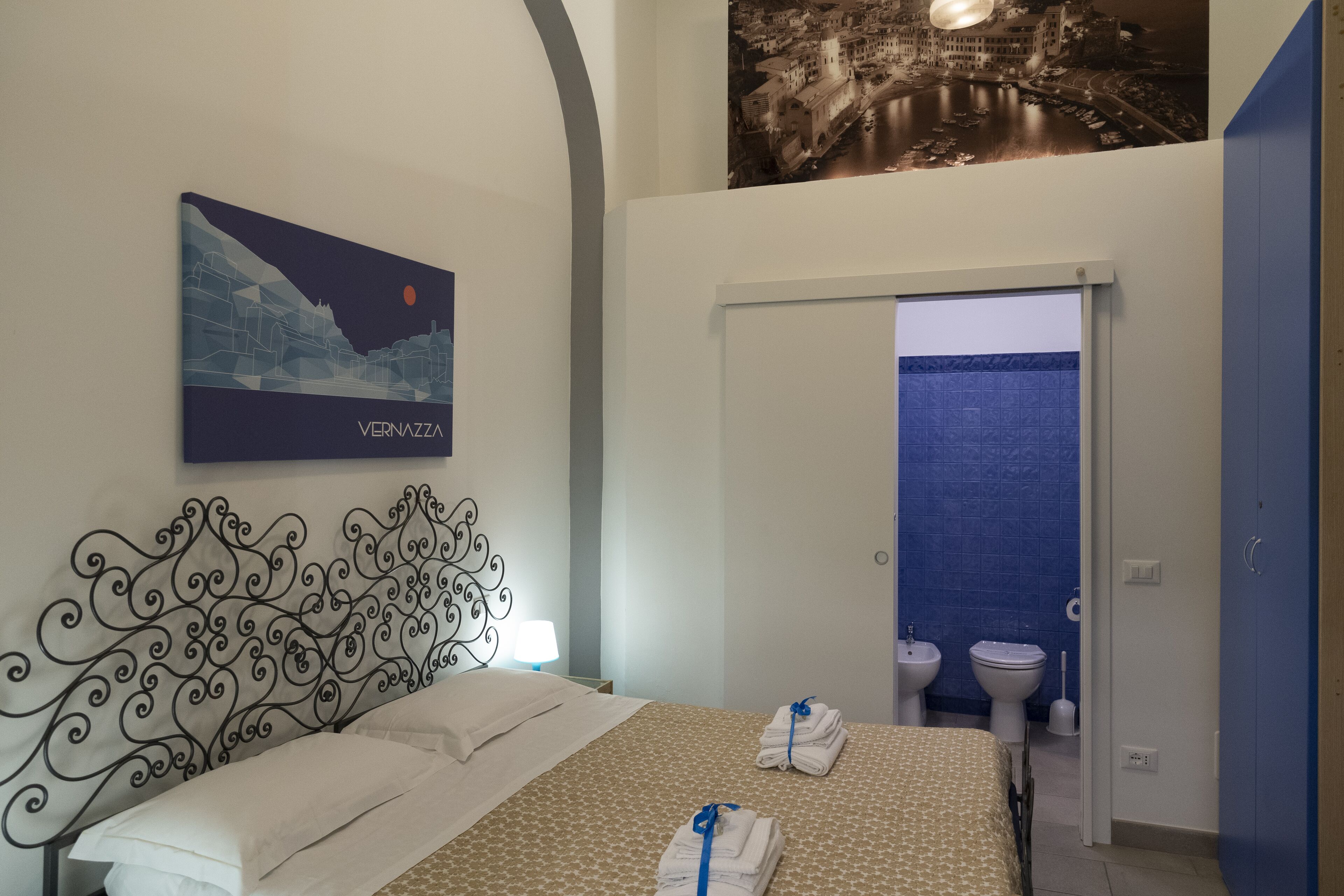 Habitación de hotel con cama, un cuadro colgado en la pared, baño visible a través de una puerta abierta y una pared de azulejos azules.
