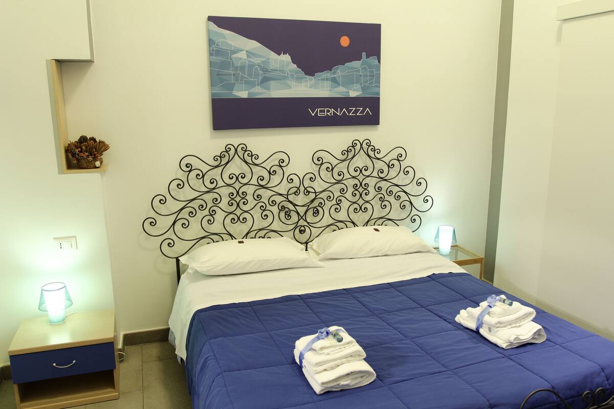 A neatly made bed with a blue bedspread and two folded towels on the side.