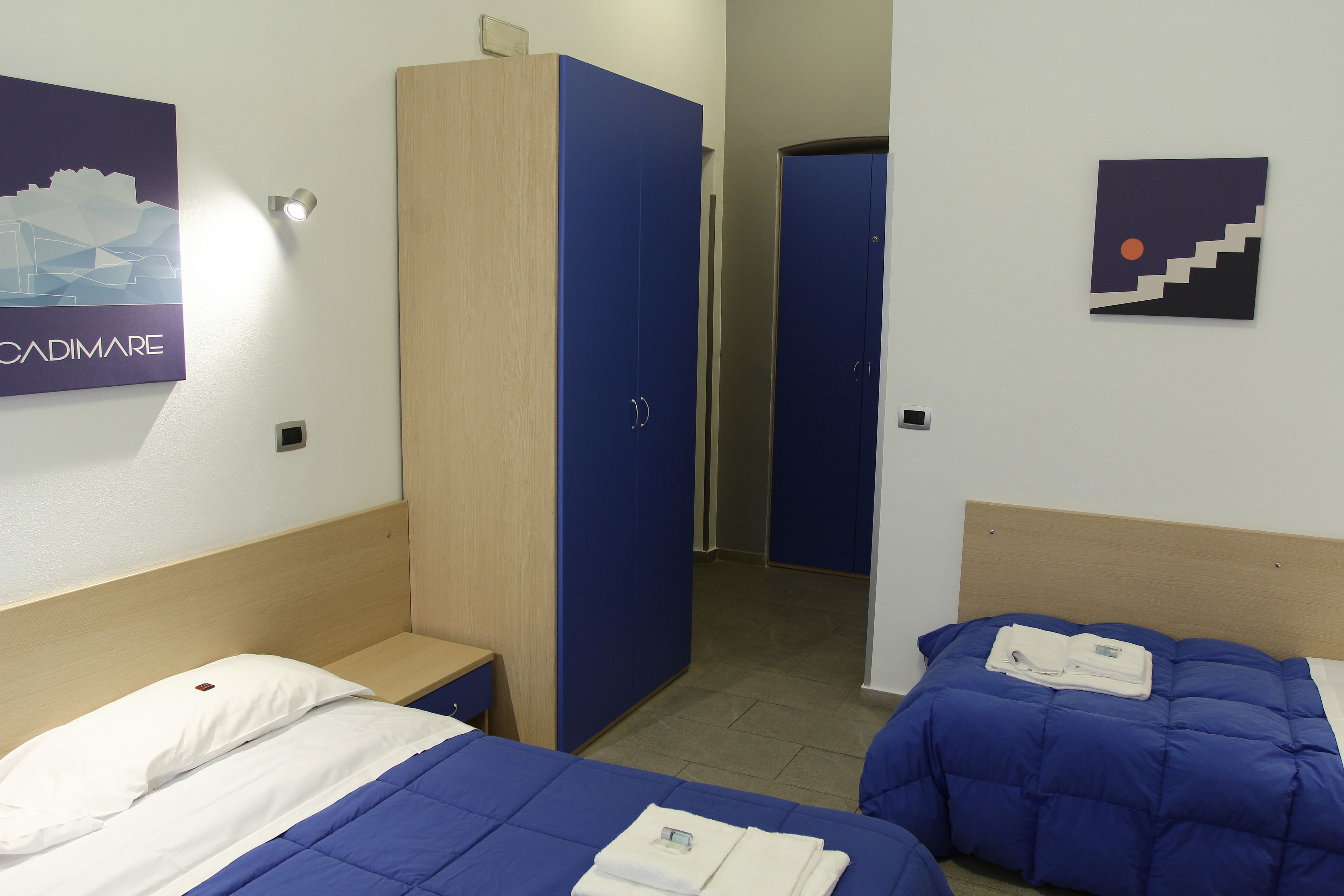 Une chambre d’hôtel avec deux lits, une armoire et une affiche au mur.