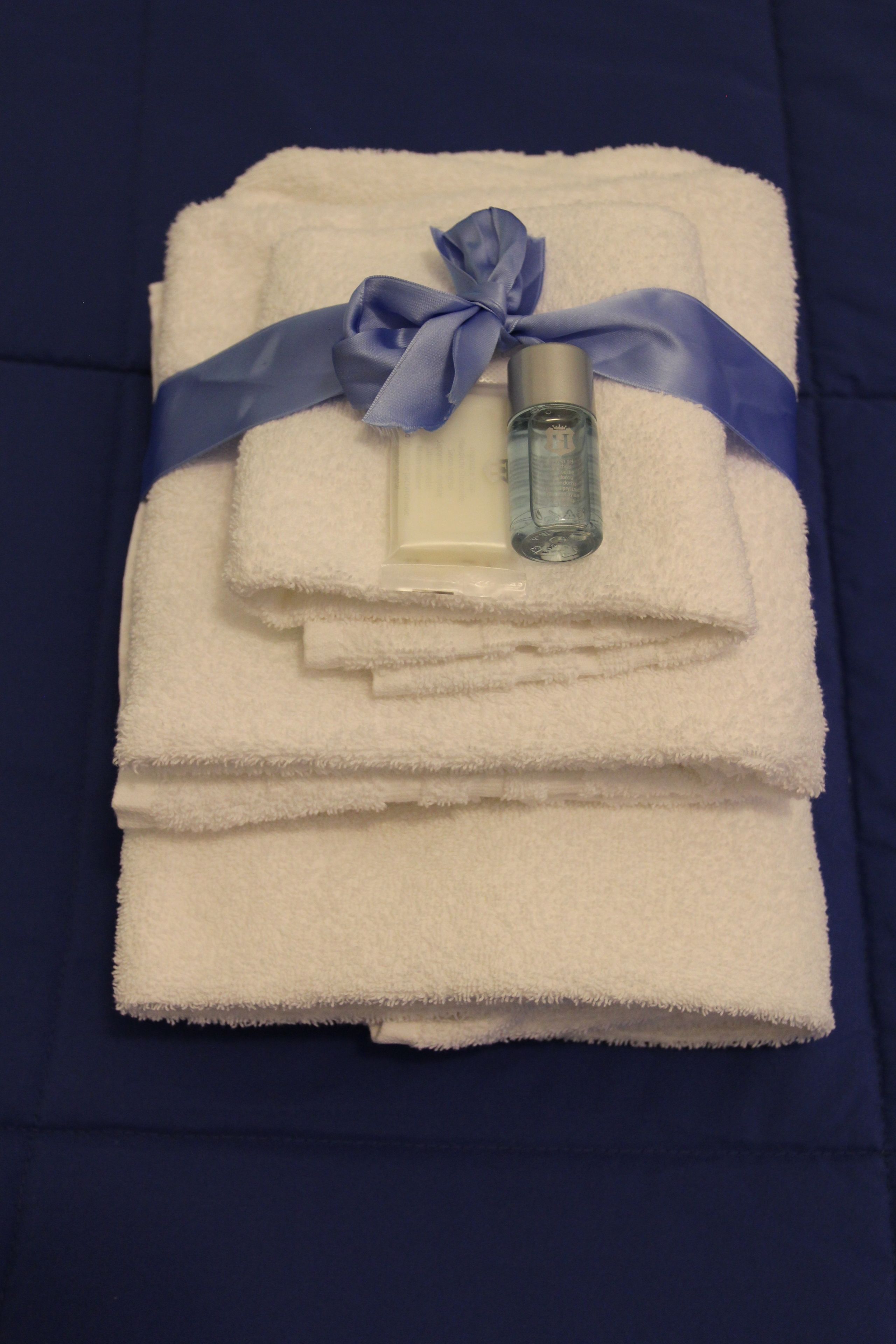 A stack of white towels with a blue ribbon and a bottle of lotion on a blue bedspread.