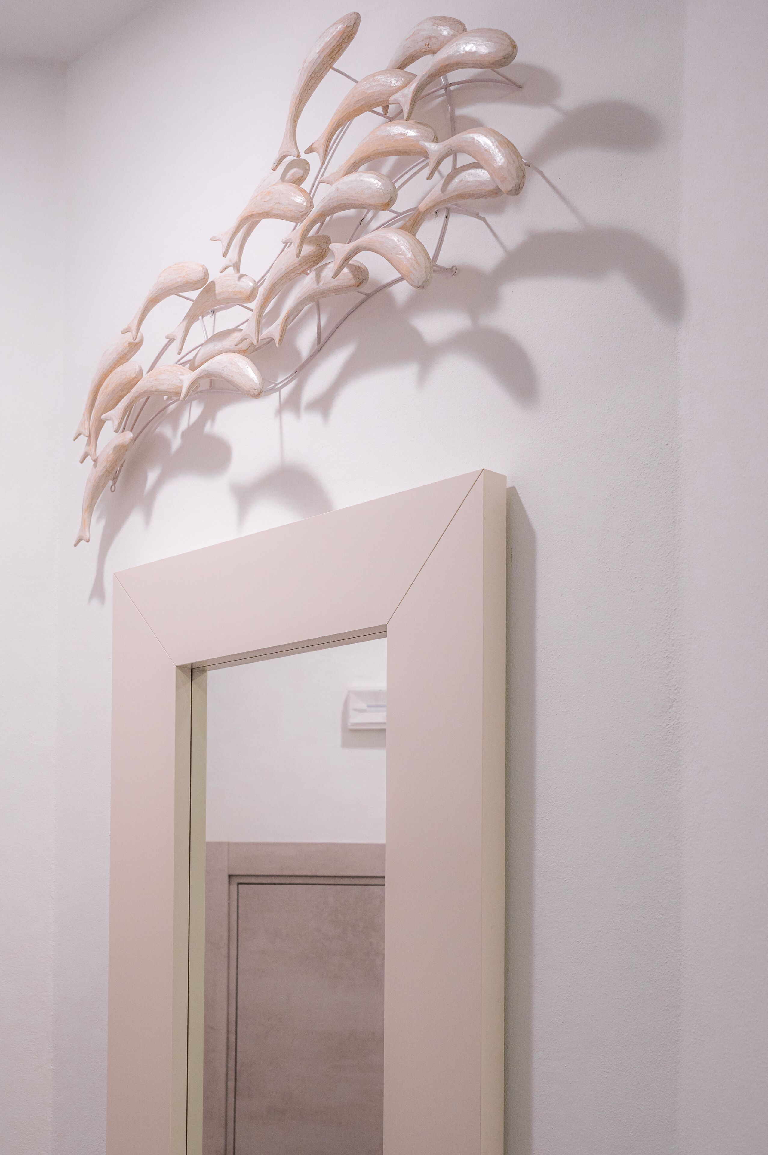 A minimalist room with a large mirror, a light-colored door, and a wall-mounted sculpture.