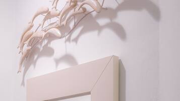 A minimalist room with a large mirror, a light-colored door, and a wall-mounted sculpture.
