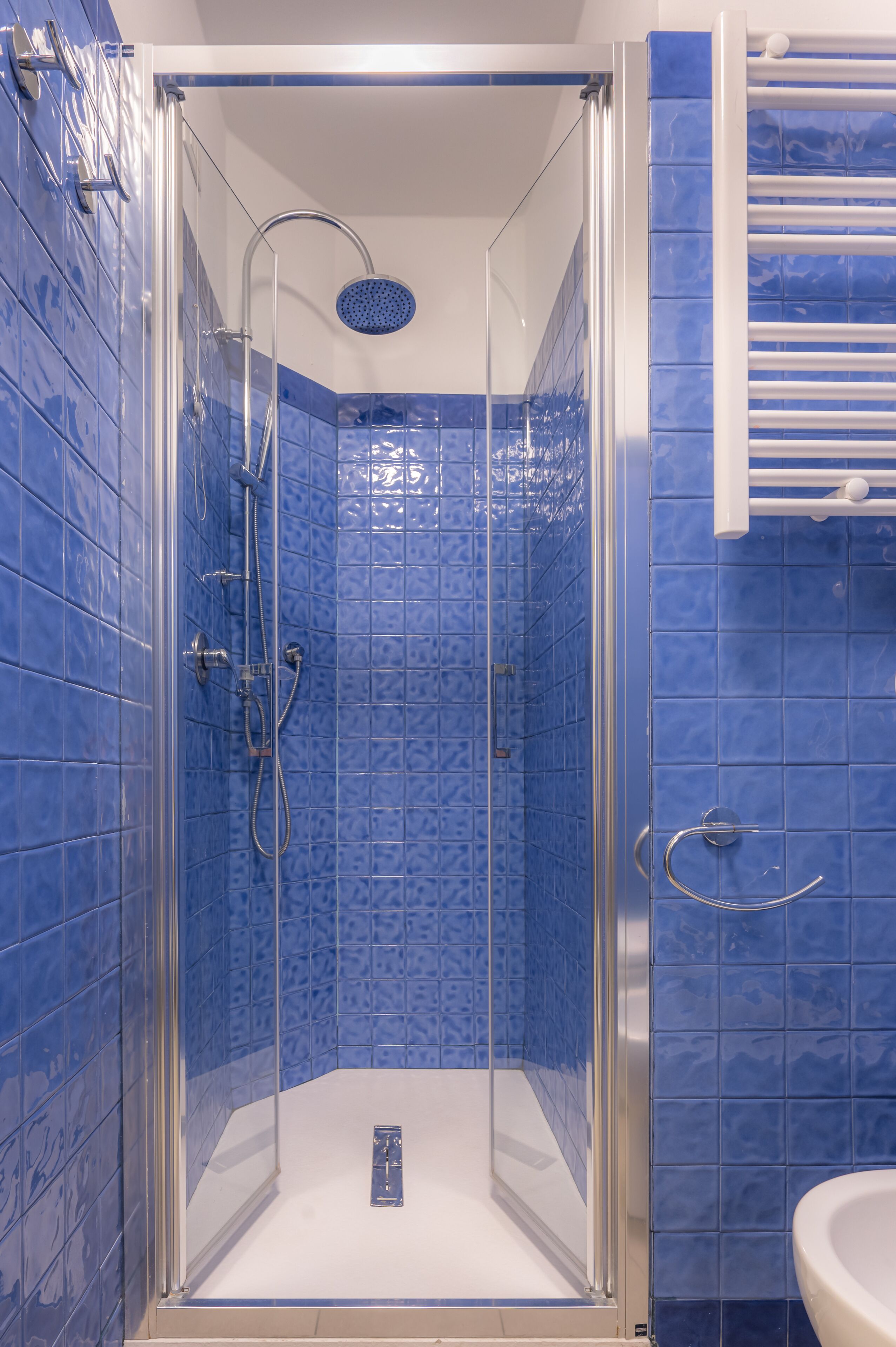 Une douche fermée par des parois de verre, avec des murs recouverts de carreaux bleus et un lavabo blanc.